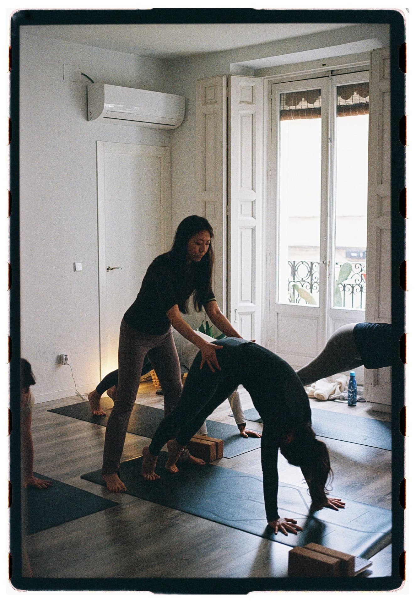 Séverine Han ajustando la postura del perro boca abajo a una alumna, sesión Jivamukti Yoga Nidra fotografía analógica Madrid