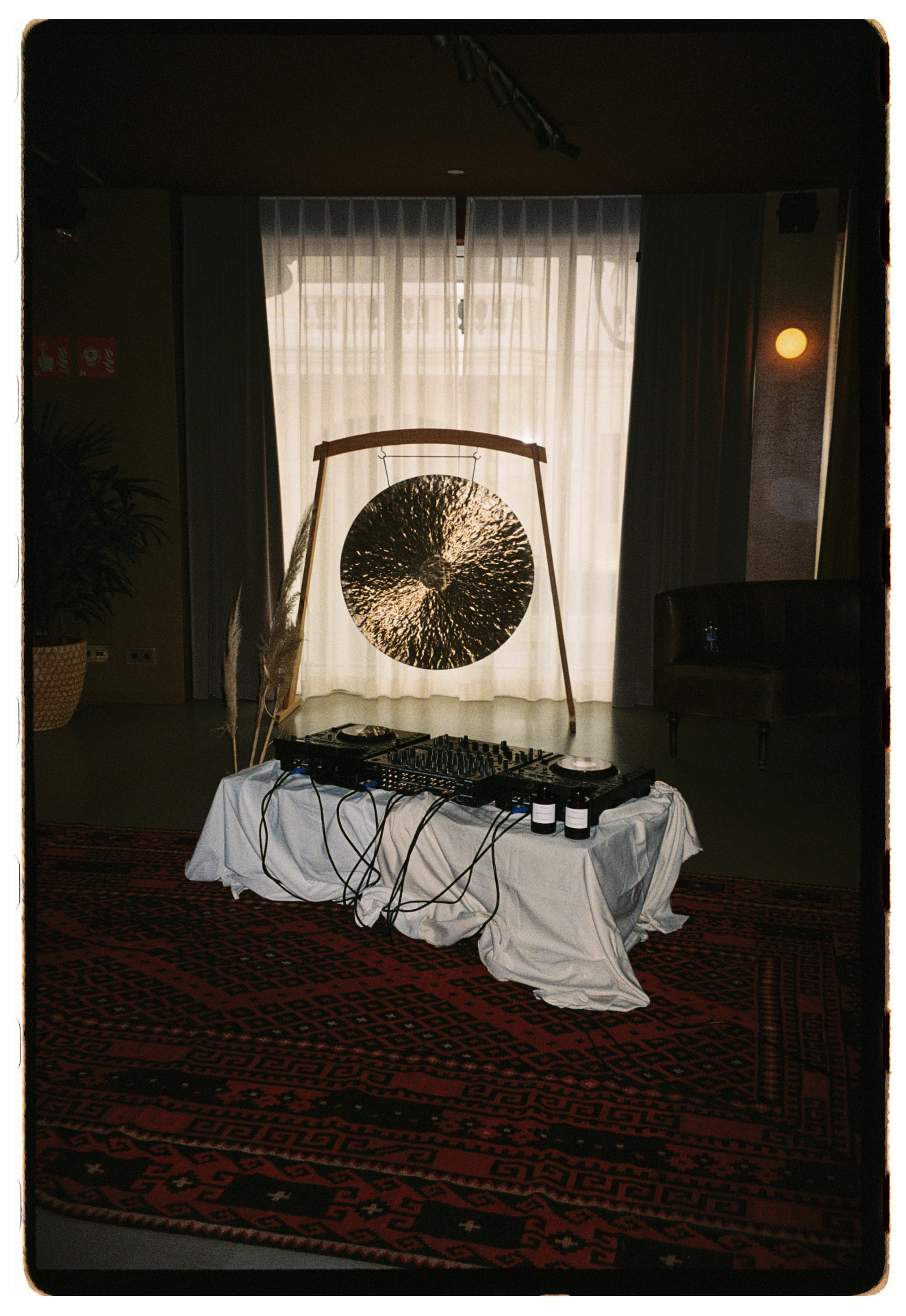 Gong dorado a contraluz sobre cortinas blancas con cabina de DJ en primer plano, La Siesta Hotel Nomade Madrid fotografía analógica