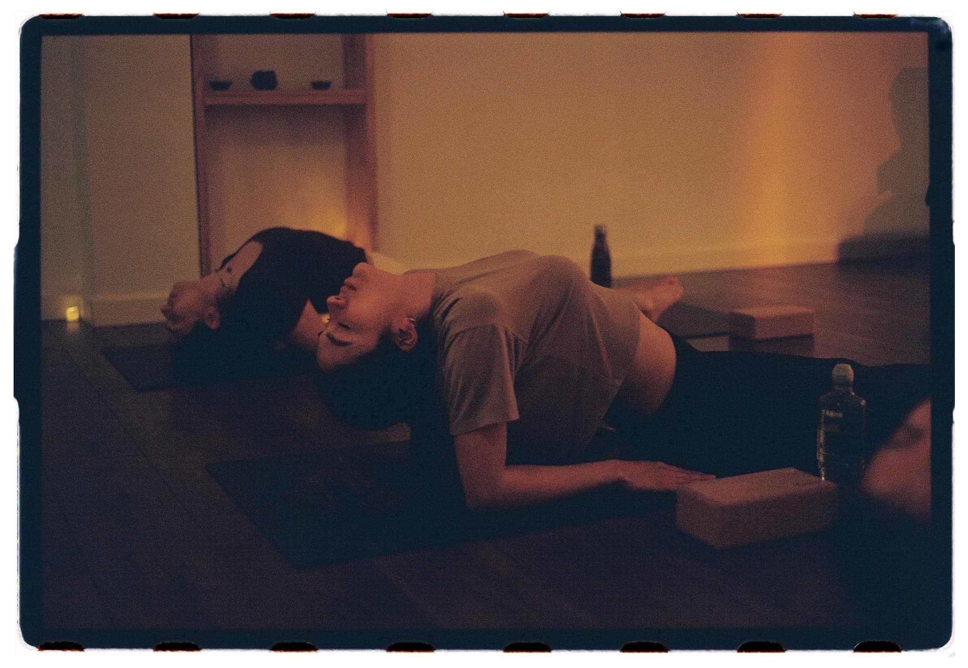 Alumnos en savasana lateral bajo luz ámbar al cierre de la sesión, práctica vinyasa Laura Fernández fotografía analógica Madrid