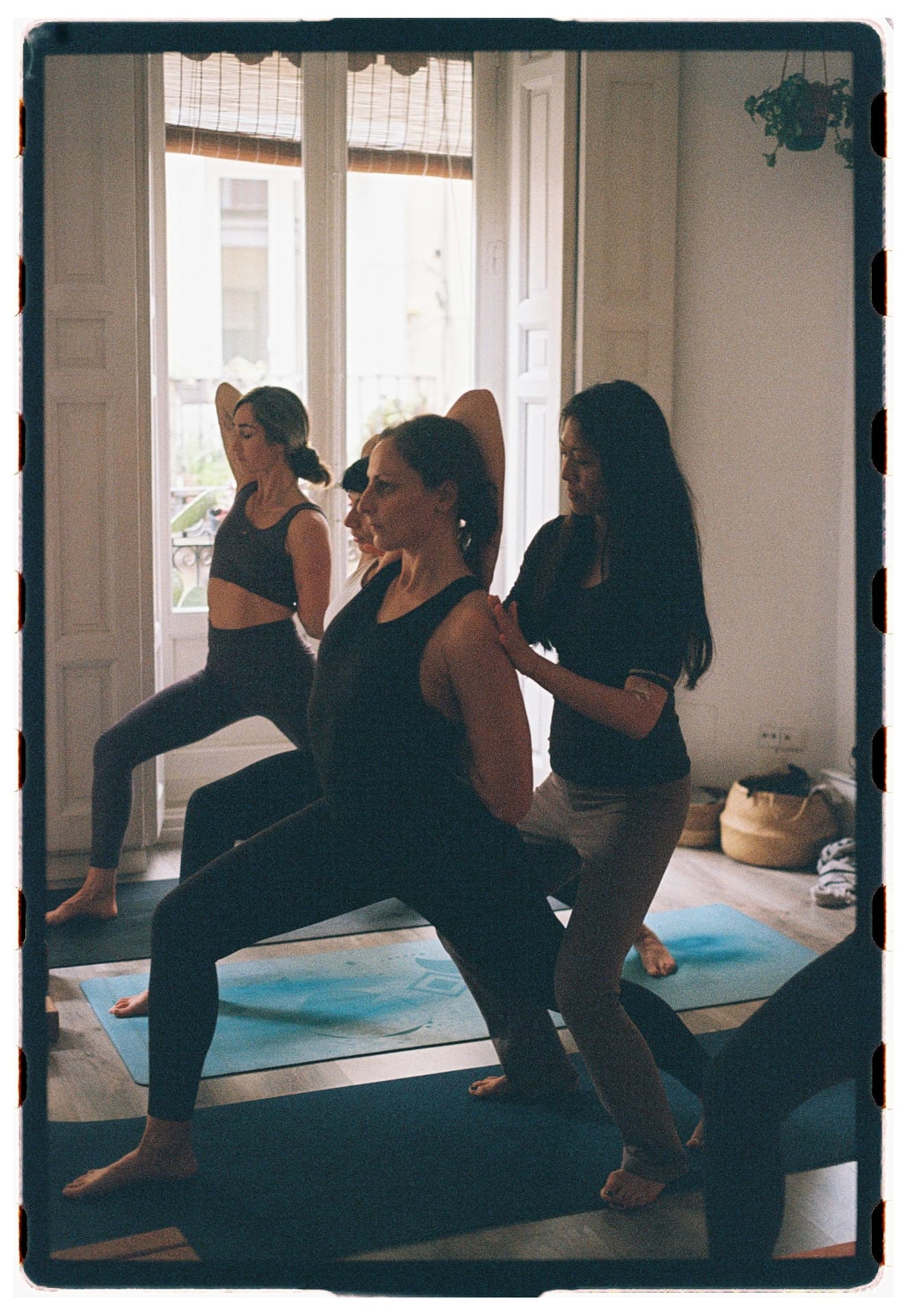 Alumnas en postura del guerrero con asistencia manual de la profesora, sesión Jivamukti Yoga Nidra fotografía analógica Madrid