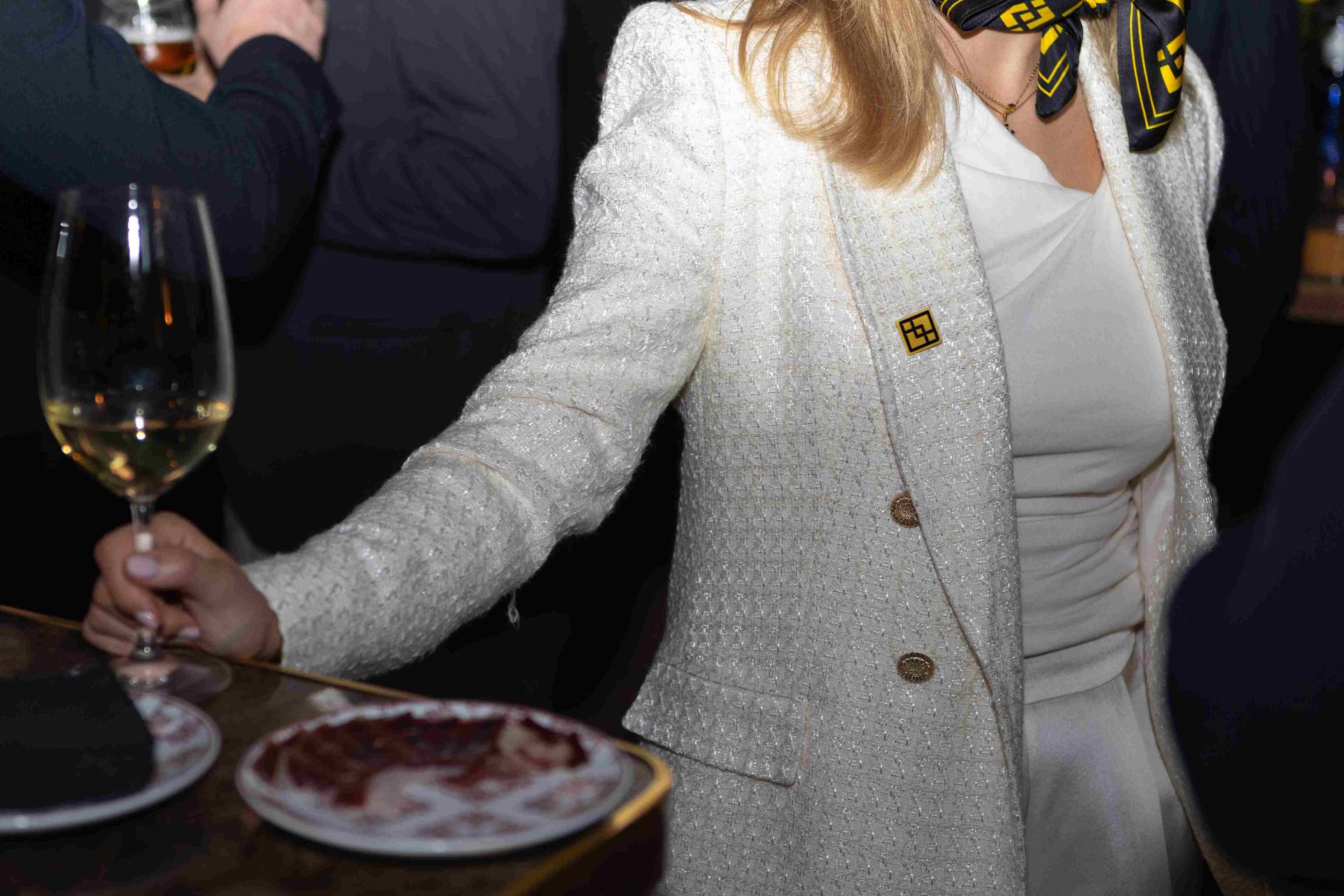 Detalle del pin de Binance y copa de vino blanco sobre la mesa del cóctel en Tatel Madrid