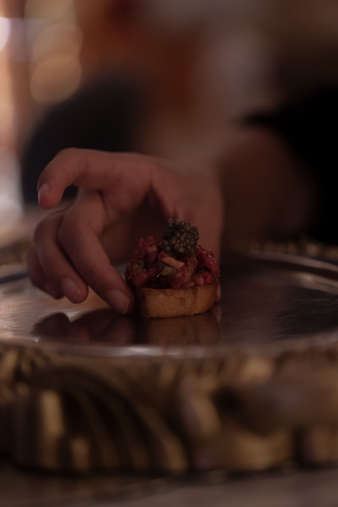 Mano ofreciendo tosta de tartar con caviar en el servicio del restaurante Manero Madrid