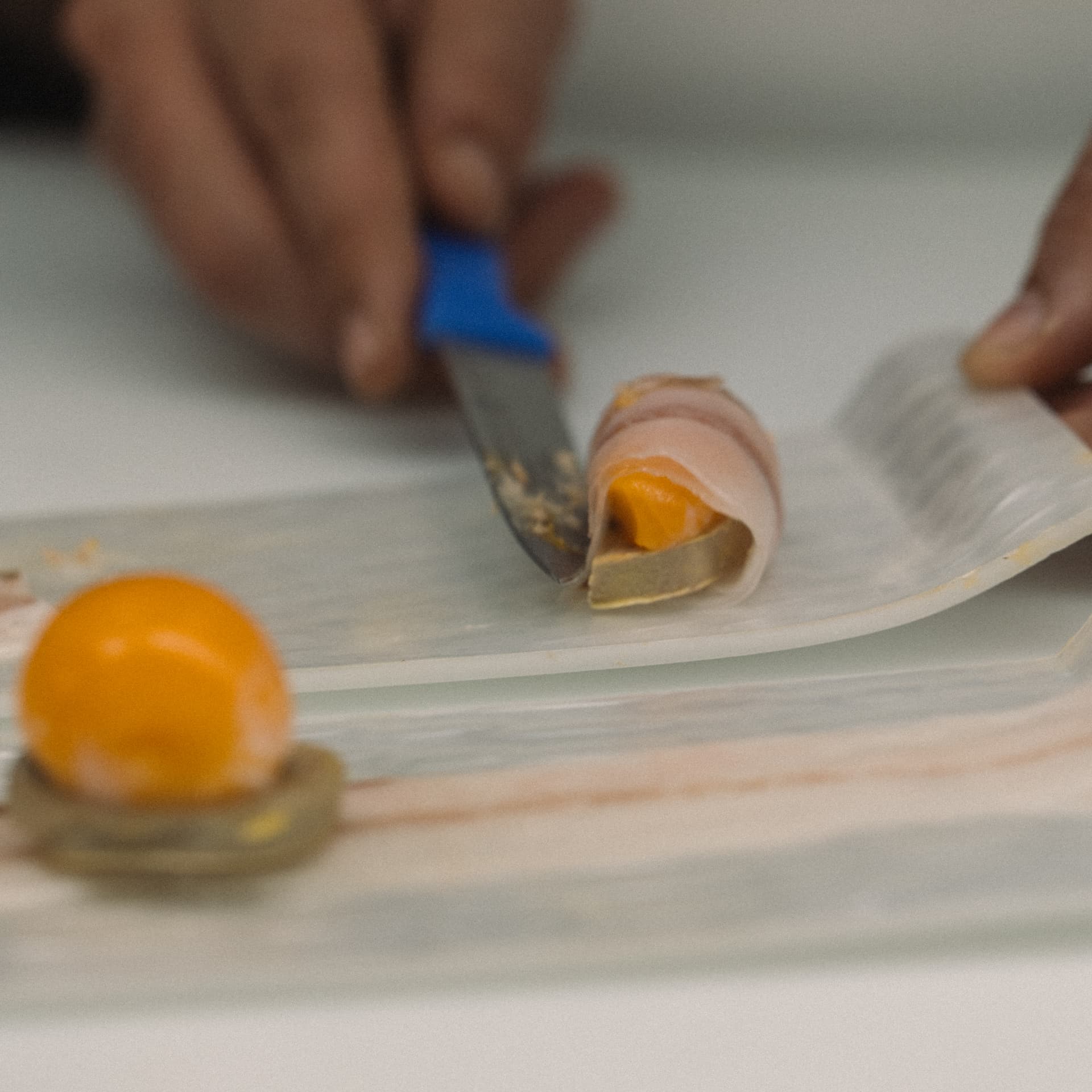 Corte de yema curada envuelta en jamón durante el emplatado final en barra en Sala de Despiece