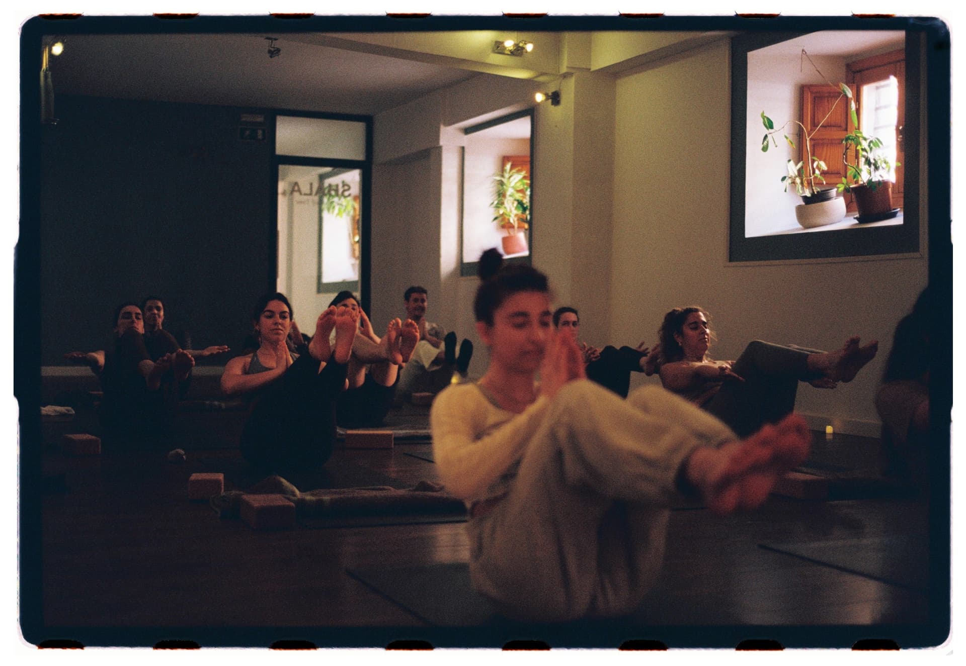 Alumnos en navasana con la profesora borrosa en primer plano, práctica vinyasa Laura Fernández fotografía analógica Madrid