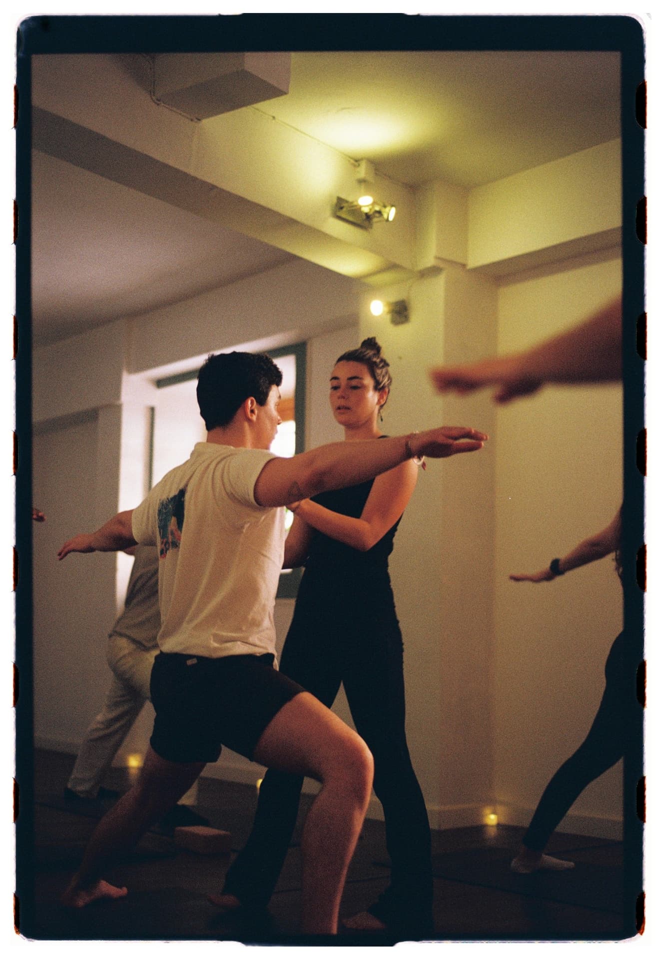 Laura Fernández ajustando el brazo de un alumno en warrior II durante la clase, práctica vinyasa fotografía analógica Madrid