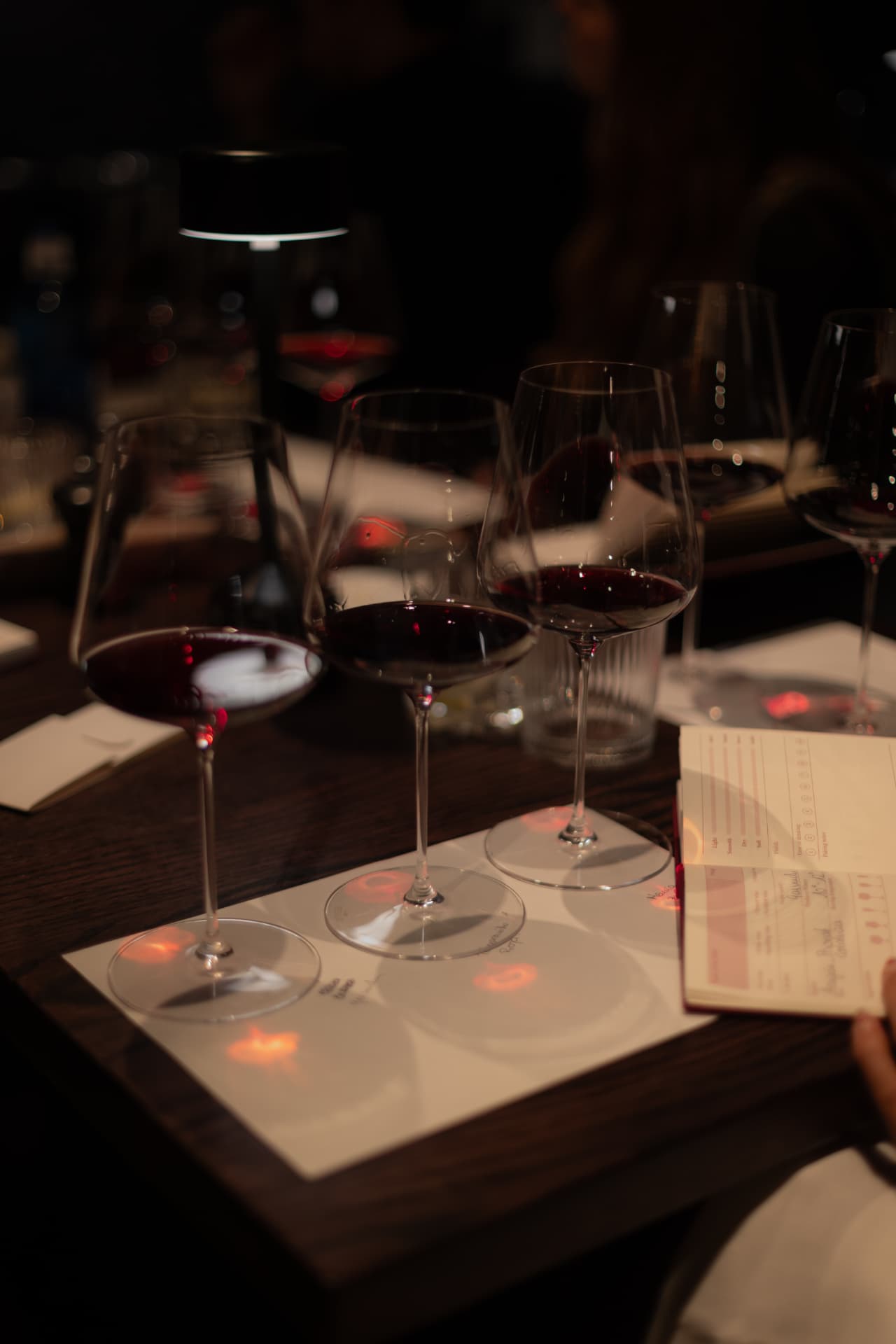 Cata de tres copas de vino tinto con lámpara de mesa en la bodega de Roostiq Bar Madrid