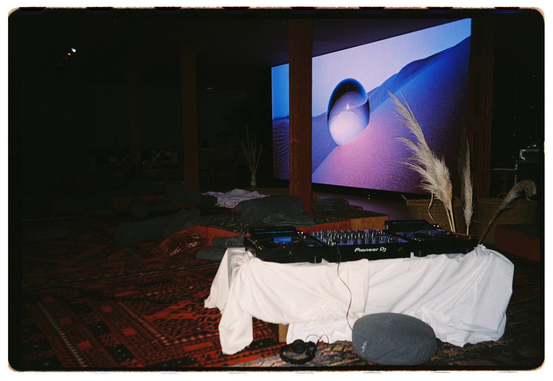 Sala en penumbra con proyección de dunas y setup de DJ vestido de blanco, La Siesta Hotel Nomade Madrid fotografía analógica