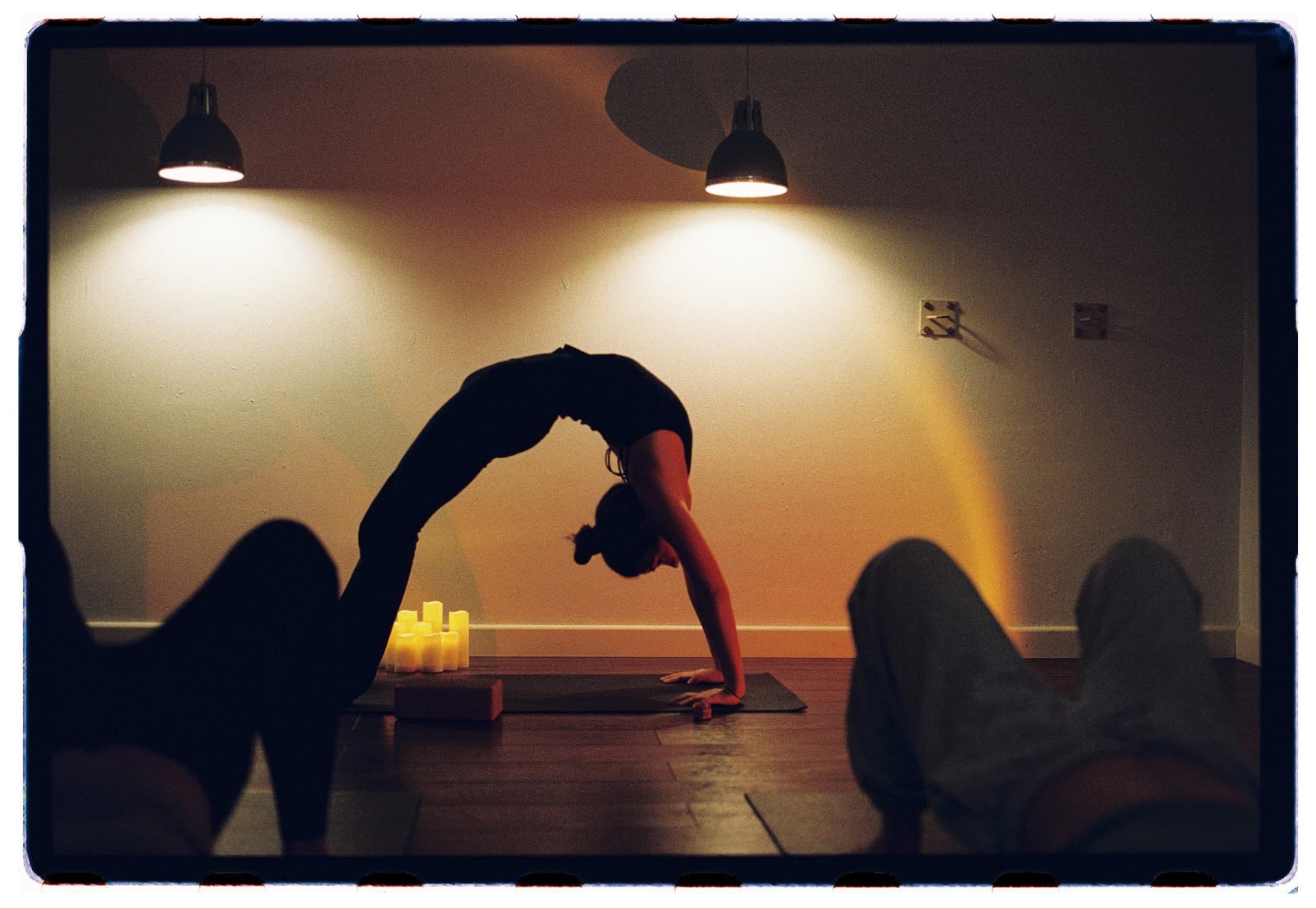 Silueta de alumna en urdhva dhanurasana bajo luz cálida entre velas, práctica vinyasa Laura Fernández fotografía analógica Madrid