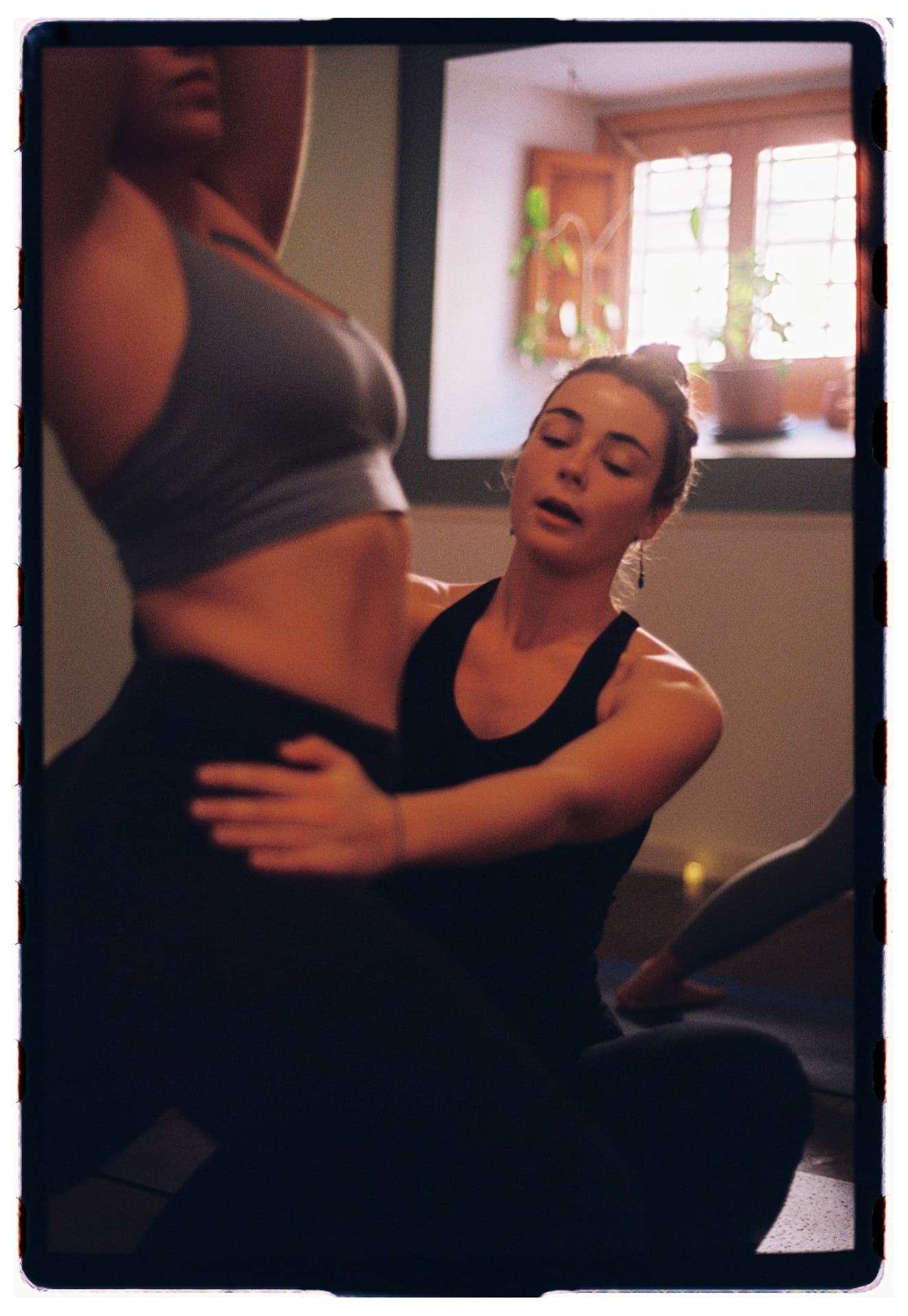 Laura Fernández asistiendo manualmente el torso de una alumna sentada, práctica vinyasa fotografía analógica Madrid