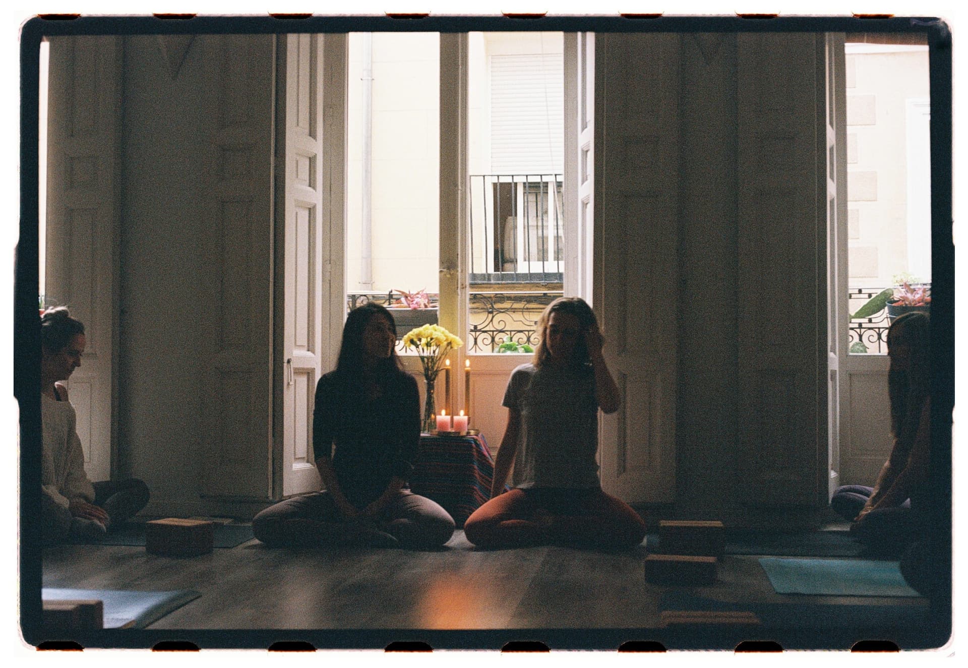 Alumnas sentadas en meditación frente al balcón con velas encendidas, sesión Jivamukti Yoga Nidra fotografía analógica Madrid