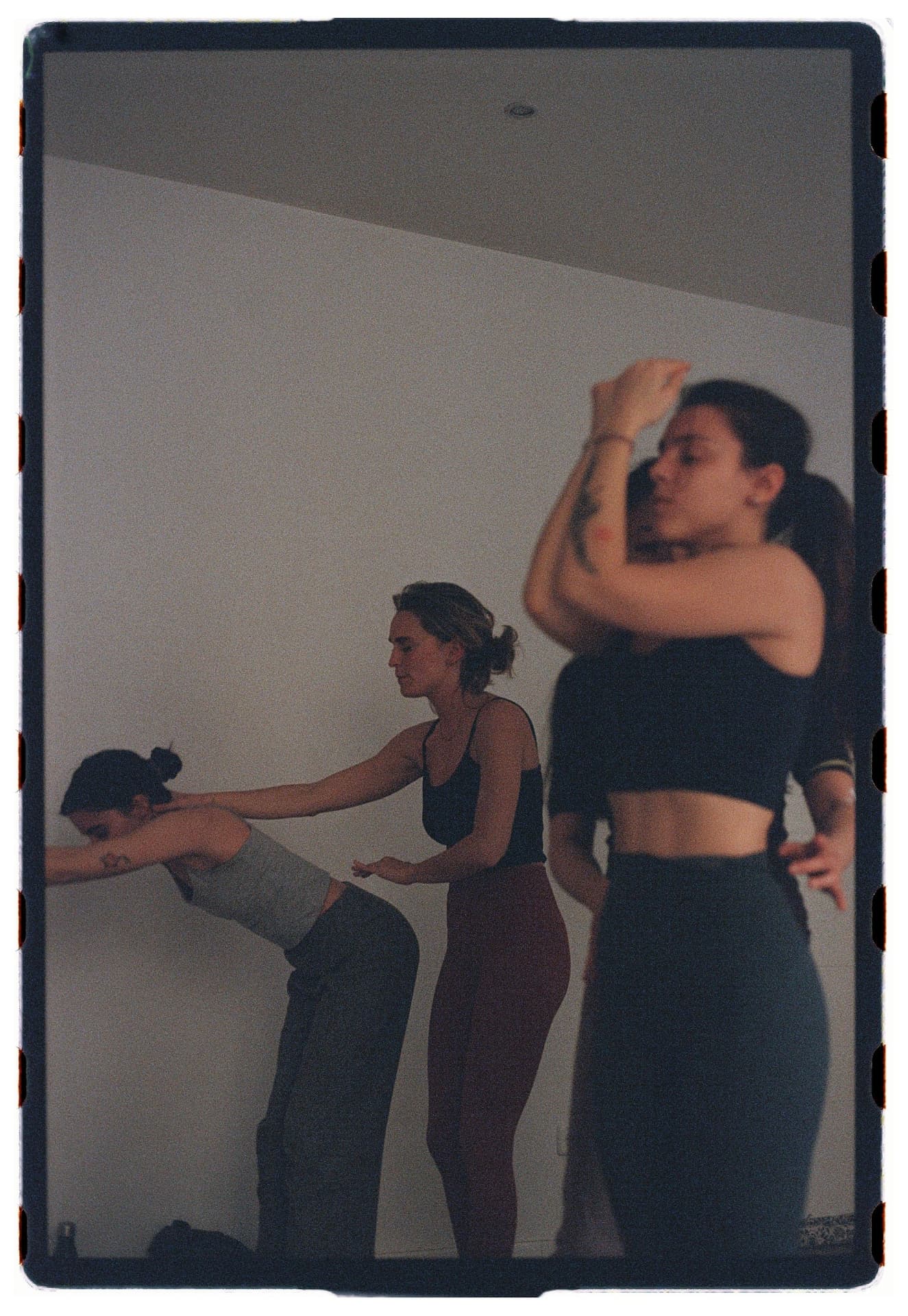 Profesora ajustando la postura de una alumna junto a otras practicantes de pie, sesión Jivamukti Yoga Nidra fotografía analógica Madrid