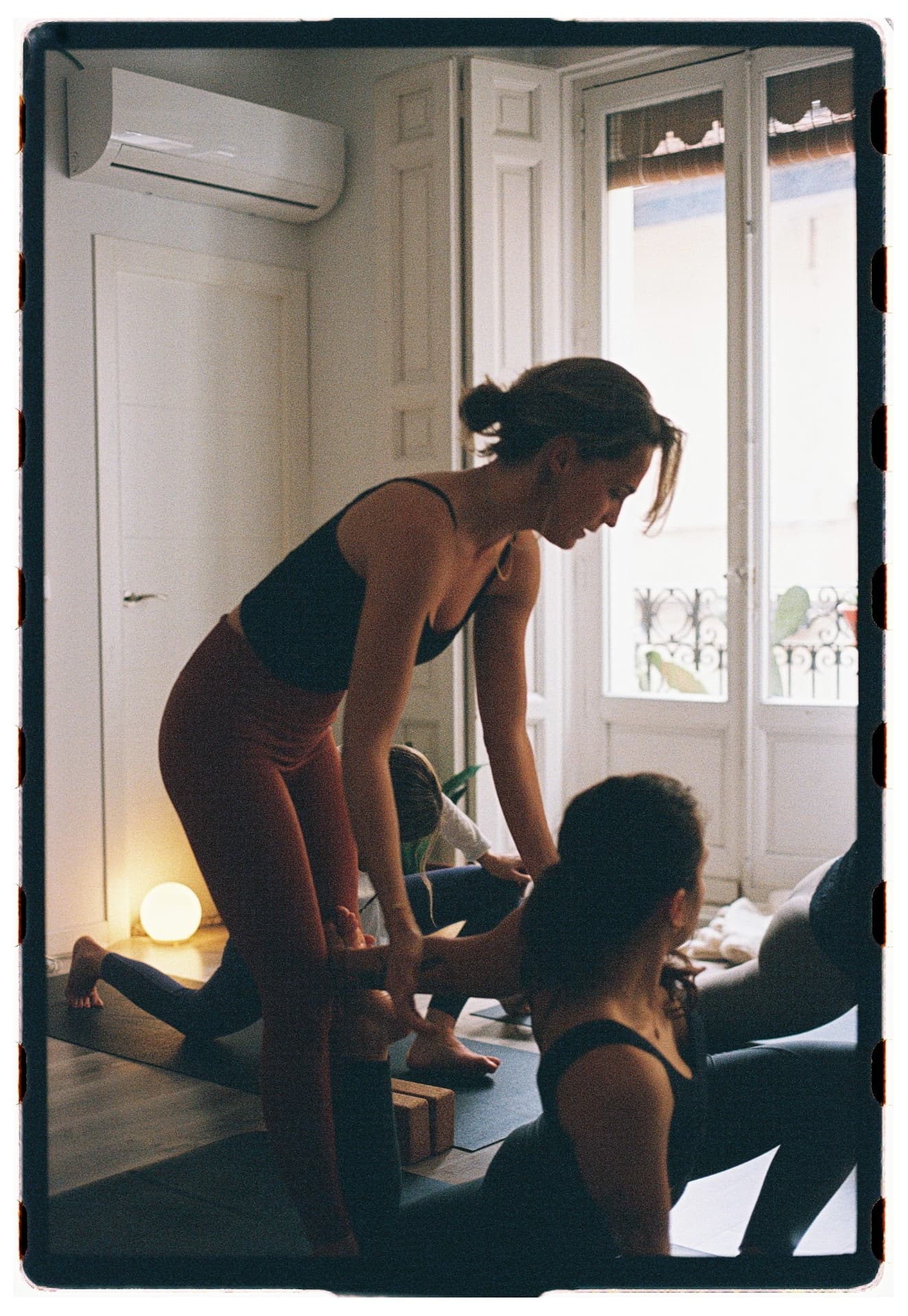 Cristina Sagües asistiendo a una alumna en postura de pie durante la práctica, sesión Jivamukti Yoga Nidra fotografía analógica Madrid