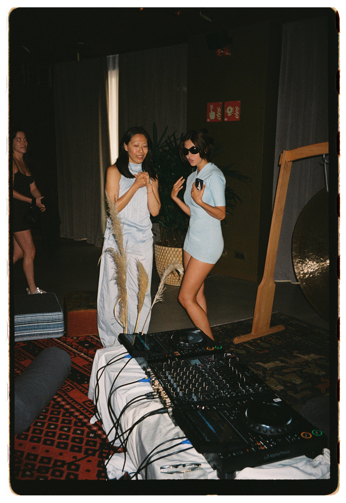 DJs bailando junto a la mesa de mezclas con pampas y gong al fondo, La Siesta Hotel Nomade Madrid fotografía analógica