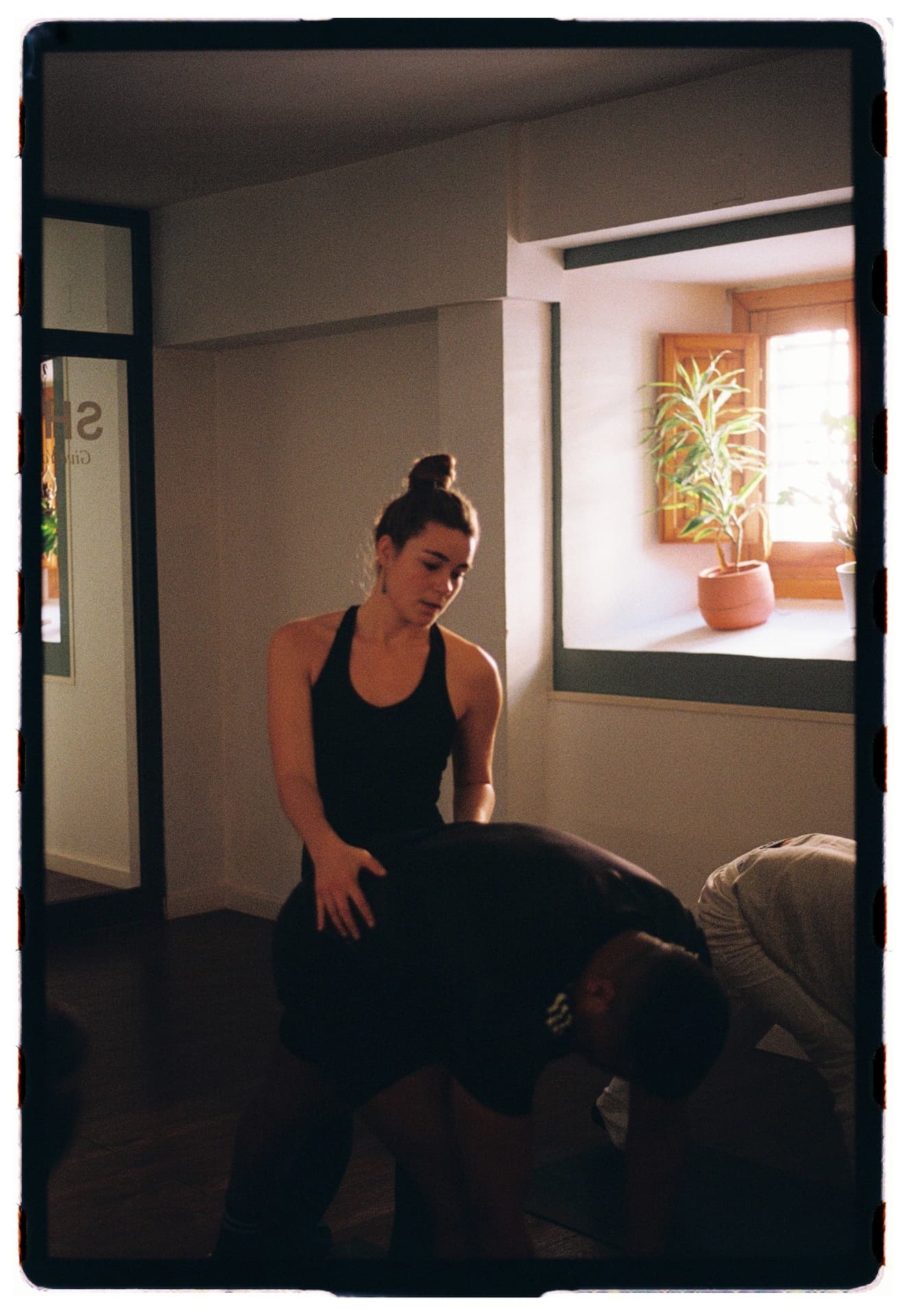 Profesora acompañando la postura del niño de un alumno junto a la ventana, práctica vinyasa Laura Fernández fotografía analógica Madrid