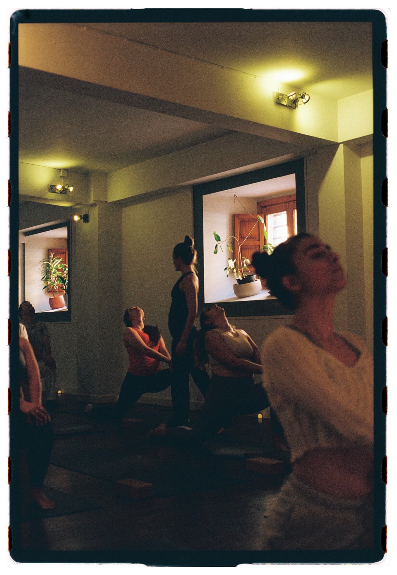 Grupo en warrior con silueta borrosa en primer plano, práctica vinyasa Laura Fernández fotografía analógica Madrid