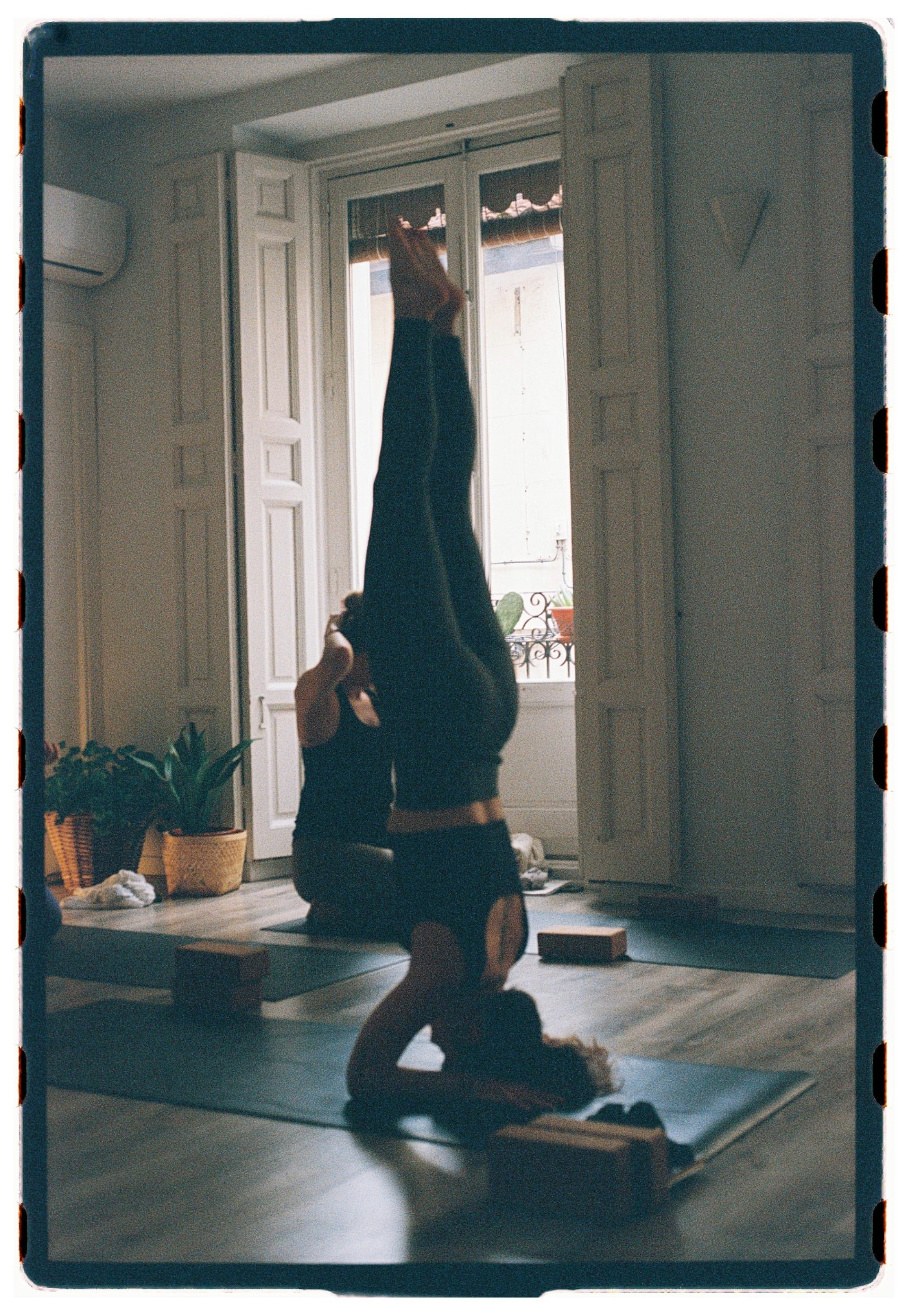 Alumna en postura invertida sobre la cabeza con piernas alineadas hacia el techo, sesión Jivamukti Yoga Nidra fotografía analógica Madrid