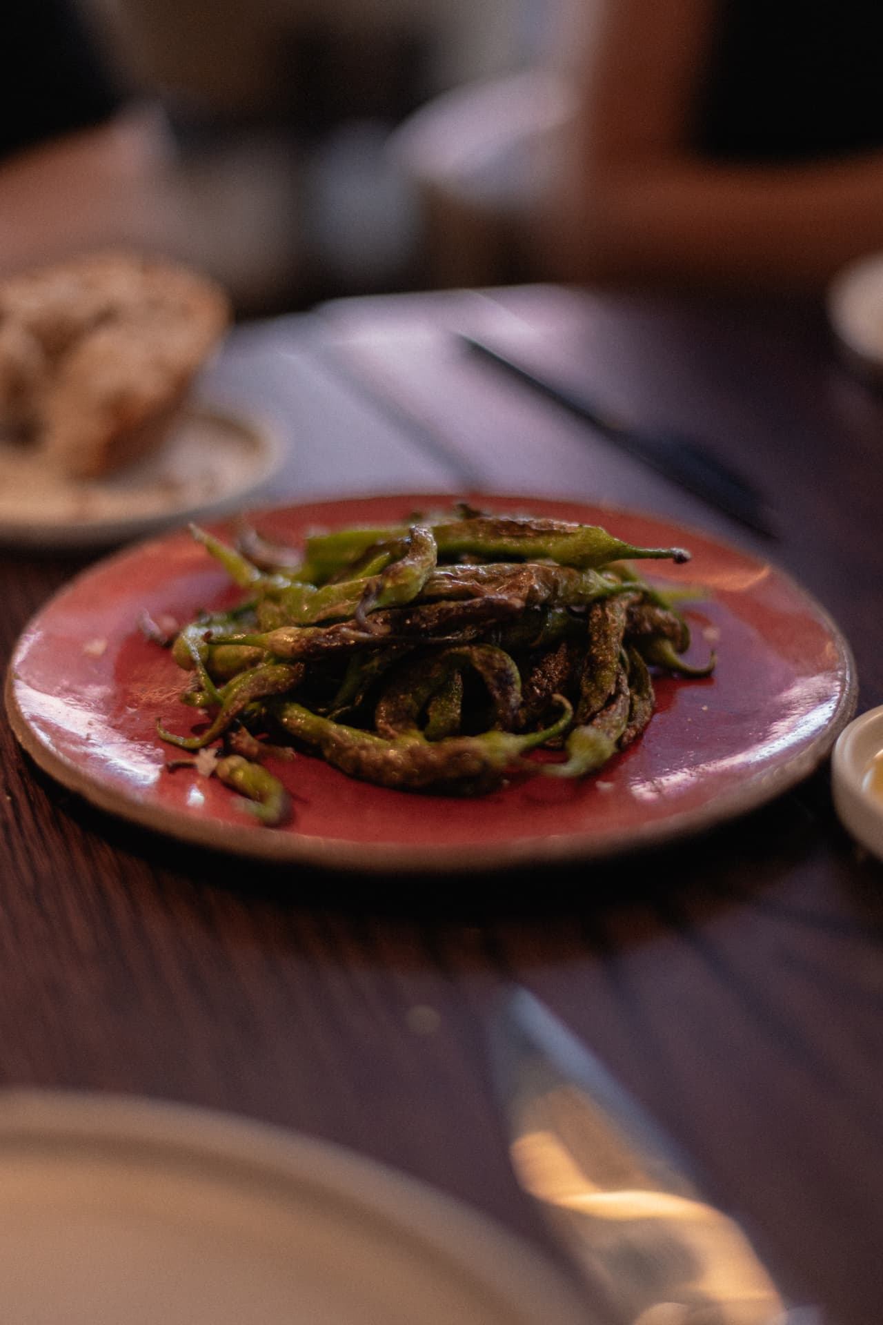 Pimientos de padrón fritos sobre plato rojo en Roostiq Bar Madrid